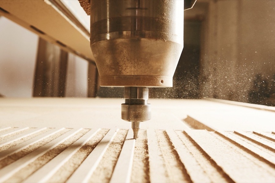CNC router spindle machining parallel grooves into a timber board, dust lifting off the cut